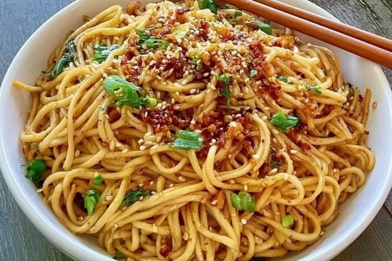 A vibrant bowl of Garlic Sesame Noodles garnished with sesame seeds and green onions.